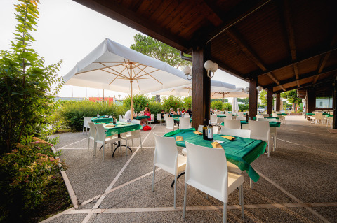 Zona de comedor exterior en Campeggio del Garda, con manteles verdes, sombrillas y sillas blancas en Véneto, Italia.