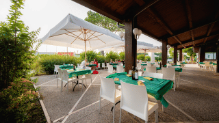 Zona de comedor exterior en Campeggio del Garda, con manteles verdes, sombrillas y sillas blancas en Véneto, Italia.