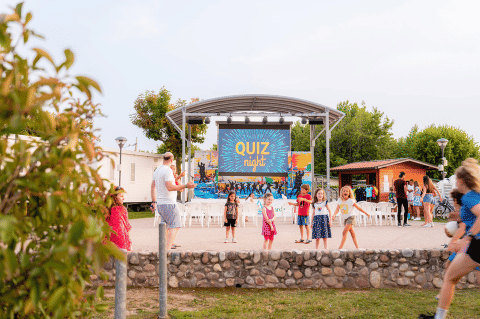 Kinder spielen vor einer Bühne mit 'Quiz Night' im Campeggio del Garda Ferienpark in Venetien, Italien.