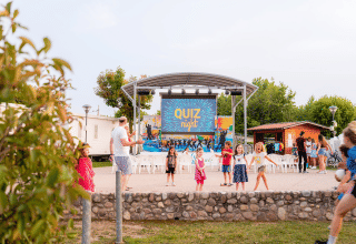 Kinder spielen vor einer Bühne mit 'Quiz Night' im Campeggio del Garda Ferienpark in Venetien, Italien.