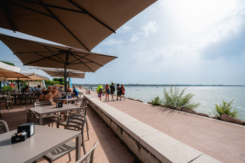 Café en plein air au bord du lac à Campeggio del Garda, Vénétie, Italie, avec clients sous grands parasols.