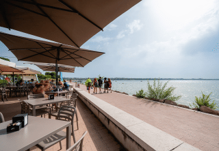 Café al aire libre junto al lago en Campeggio del Garda, Véneto, Italia, con huéspedes bajo grandes sombrillas.