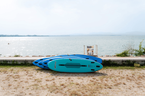 Four blue paddleboards on the ground near a lake at Campeggio del Garda, Veneto, Italy, with water in view.