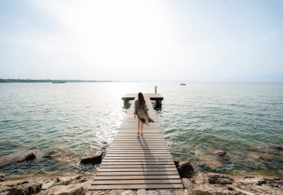 Frau spaziert auf einem Holzsteg am Wasser in Campeggio del Garda, Venetien, Italien, bei Sonnenschein.