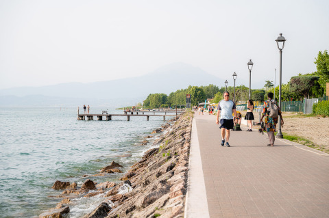 Menschen spazieren auf der Uferpromenade von Campeggio del Garda in Venetien, Italien, bei Sonnenschein.