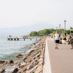 Personas pasean por el paseo junto al lago en Campeggio del Garda, Veneto, Italia, en un día soleado.