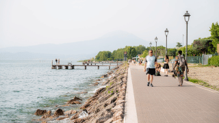 Personas pasean por el paseo junto al lago en Campeggio del Garda, Veneto, Italia, en un día soleado.