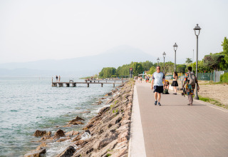 Persone passeggiano sul lungolago di Campeggio del Garda, Veneto, Italia, in una giornata di sole.