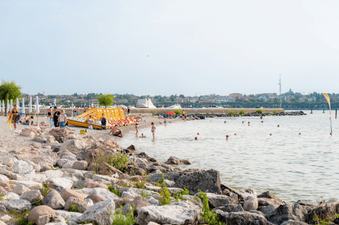 Strand im Campeggio del Garda, Veneto, Italien, mit Badegästen, Felsen und Freizeitaktivitäten.