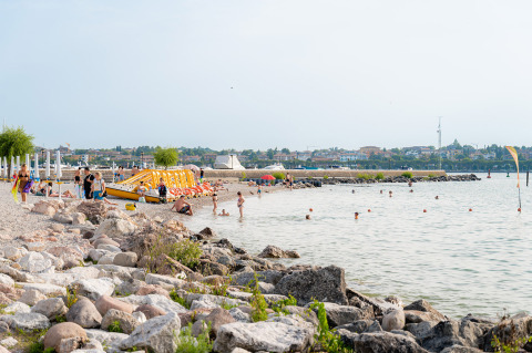 Plage au Campeggio del Garda, Vénétie, Italie, avec baigneurs, rochers et ambiance estivale.