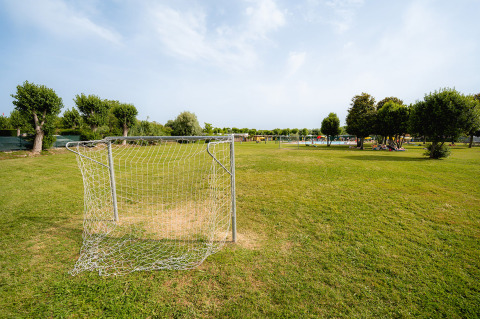 Portería de fútbol en césped verde del parque vacacional Campeggio del Garda en Véneto, Italia, con árboles.