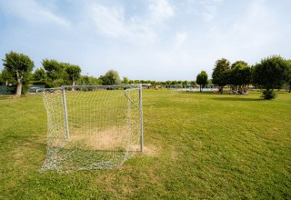 Portería de fútbol en césped verde del parque vacacional Campeggio del Garda en Véneto, Italia, con árboles.