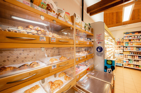 Section boulangerie d'un magasin avec croissants et pâtisseries en étagères bois, produits laitiers au fond.