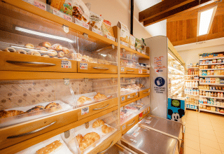 Bakery section of a store with croissants and pastries in wooden shelves, dairy products in the background.