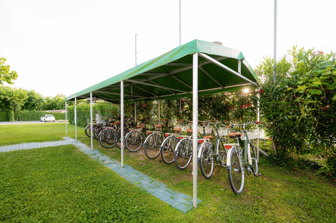 Ricovero bici con biciclette a noleggio sotto tettoia verde a Campeggio del Garda, Veneto, Italia.