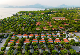 Aerial view of Campeggio del Garda holiday park in Veneto, Italy, showing cabins, trees and a nearby lake.