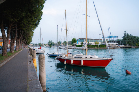 Veleros amarrados en la orilla junto al paseo y árboles en Campeggio del Garda, en Véneto, Italia.