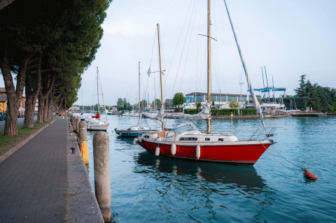 Segelboote am Ufer des Campeggio del Garda mit Promenade und Bäumen in Veneto, Italien.