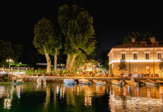 Vue nocturne avec bateaux amarrés et bâtiments illuminés au bord de l’eau à Campeggio del Garda, Vénétie, Italie.