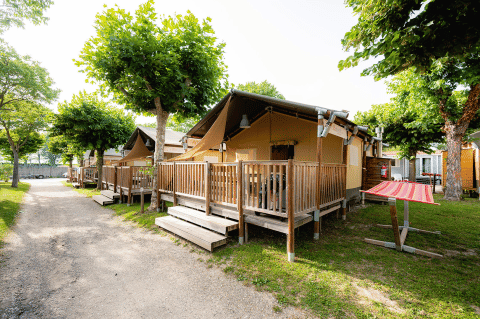 Wooden cabins and tent lodges beneath trees at Campeggio del Garda holiday park in Veneto, Italy, sunny day.