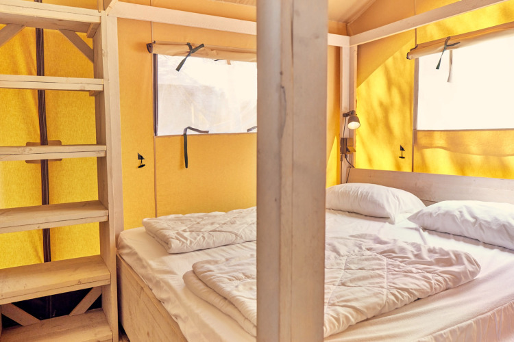 Habitación de tienda safari con cama doble y estantes de madera en Villatent Outback, Italia.