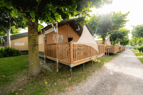 Safari tent Villatent Outback met houten veranda op Campeggio del Garda in Italië, onder schaduwrijke bomen.