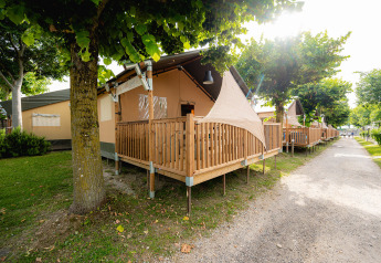 Safari tent Villatent Outback met houten veranda op Campeggio del Garda in Italië, onder schaduwrijke bomen.