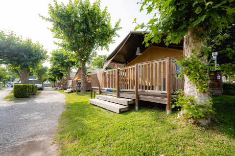 Tienda safari Villatent Outback en Campeggio del Garda, Italia, con terraza de madera y vegetación.