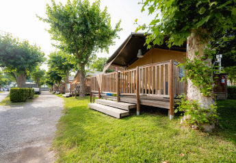 Safari tent Villatent Outback bij Campeggio del Garda in Italië met houten veranda en groene bomen.