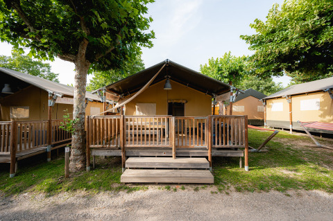 Tienda safari Villatent Outback en Campeggio del Garda, Italia, con terraza de madera y árboles verdes.