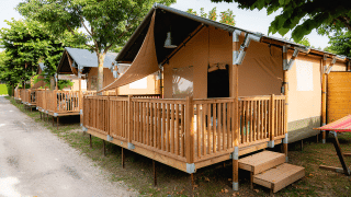 Tentes safari avec terrasse en bois à Villatent Outback, alignées sous les arbres par temps ensoleillé.