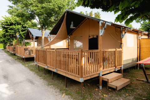 Safari tents with wooden decks at Villatent Outback, aligned under leafy trees on a sunny day.