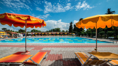 Außenpool mit bunten Liegen und Sonnenschirmen im Campeggio Gasparina, Ferienpark in Venetien, Italien.
