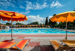 Outdoor swimming pool area with colorful loungers and umbrellas at Campeggio Gasparina, Veneto, Italy.