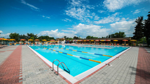 Piscina al aire libre con carriles, tumbonas y sombrillas amarillas en Campeggio Gasparina, Véneto, Italia.