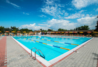 Udendørs swimmingpool med baner, solstole og gule parasoller i Campeggio Gasparina, Veneto, Italien.
