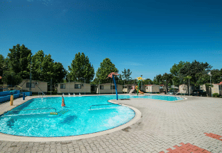 Swimming pool and holiday cabins at Campeggio Gasparina holiday park in Veneto, Italy, on a sunny day.
