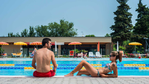Dos personas descansan junto a la piscina en Campeggio Gasparina, un parque vacacional en Véneto, Italia.