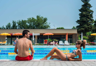 Twee personen ontspannen bij het zwembad van Campeggio Gasparina, een vakantiepark in Veneto, Italië.