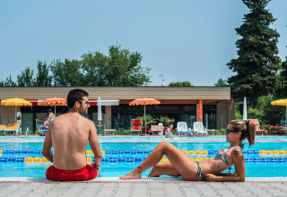 Twee personen ontspannen bij het zwembad van Campeggio Gasparina, een vakantiepark in Veneto, Italië.