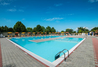 Swimmingpool og solstole med parasoller under en blå himmel i Campeggio Gasparina, Veneto, Italien.