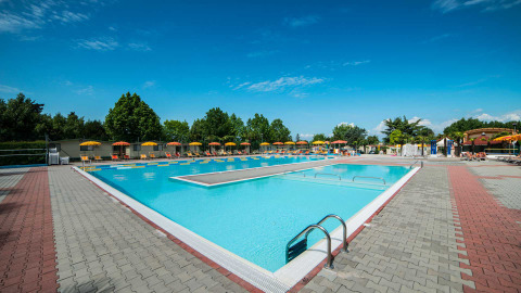 Outdoor swimming pool with sun loungers and umbrellas at Campeggio Gasparina holiday park in Veneto, Italy.