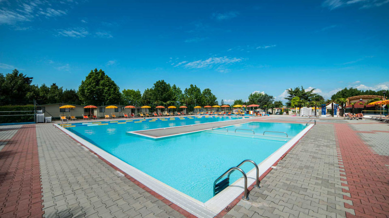 Outdoor swimming pool with sun loungers and umbrellas at Campeggio Gasparina holiday park in Veneto, Italy.