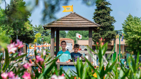 Two children playing under a wooden gazebo at Campeggio Gasparina holiday park in Veneto, Italy, with flowers.