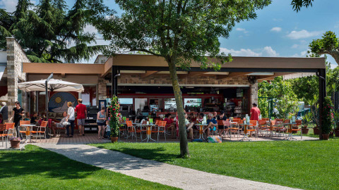 Outdoor café at Campeggio Gasparina in Veneto, Italy, with guests, green lawn, and surrounding trees.