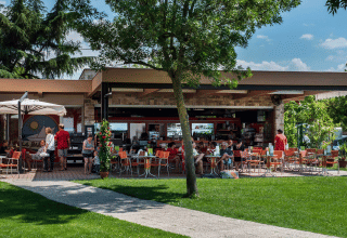 Außencafé im Campeggio Gasparina in Venetien, Italien, mit Gästen, grünem Rasen und Bäumen.