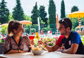 Twee vrienden klinken met drankjes op het terras van Campeggio Gasparina vakantiepark in Veneto.