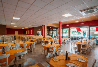 Salle de restaurant intérieure du Campeggio Gasparina en Vénétie, Italie, avec nappes orange et grandes fenêtres.