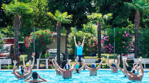 Personas haciendo aeróbic acuático en una piscina al aire libre rodeada de palmeras en Campeggio Gasparina, Veneto.