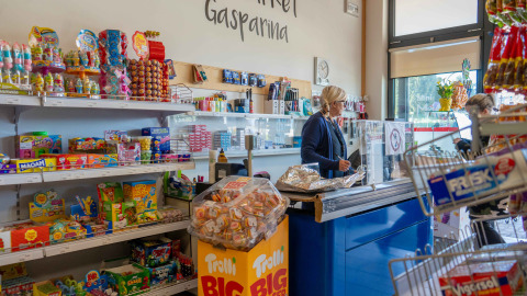 Winkelinterieur bij Campeggio Gasparina, Veneto, Italië, met snoeprekken en een kassamedewerkster.